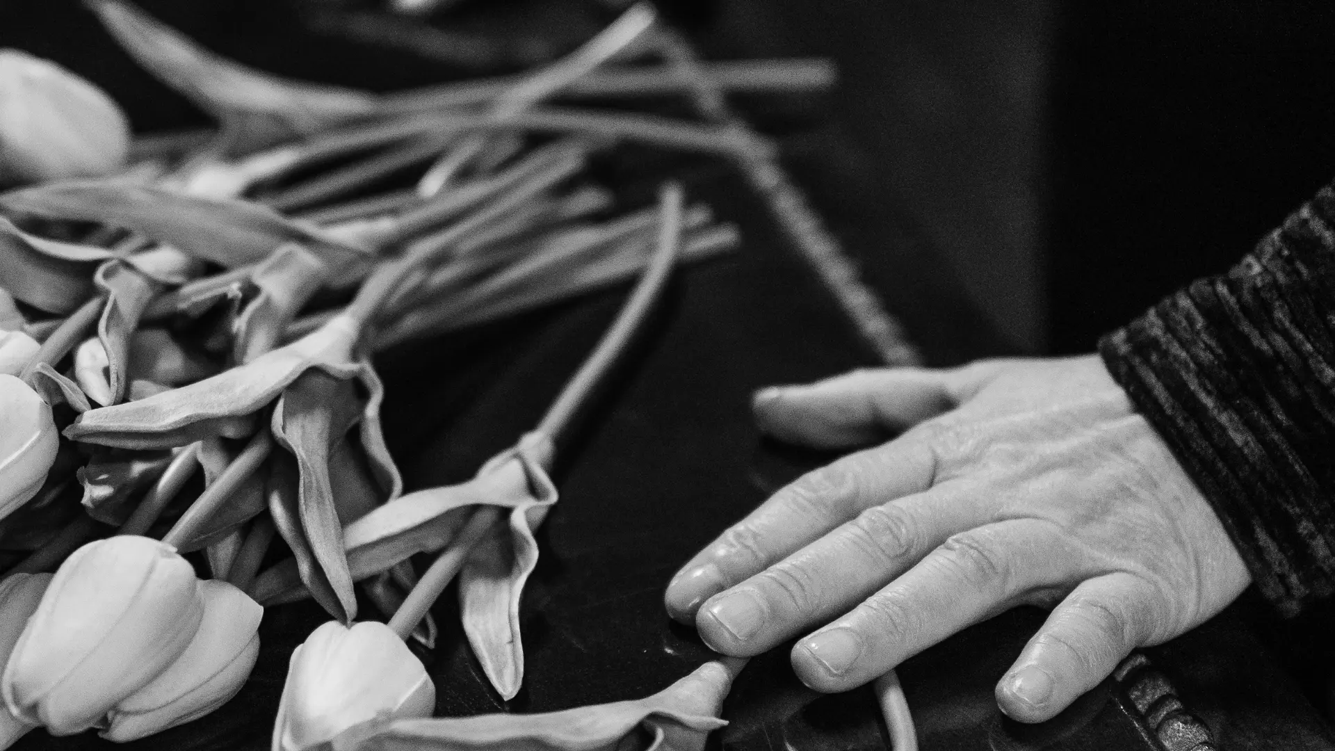 Un homme pose sa main sur un cercueil à coté d'un bouquet de fleur.